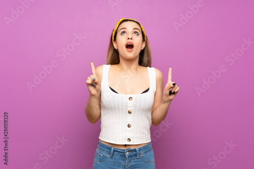 Pretty young woman over isolated purple wall surprised and pointing up