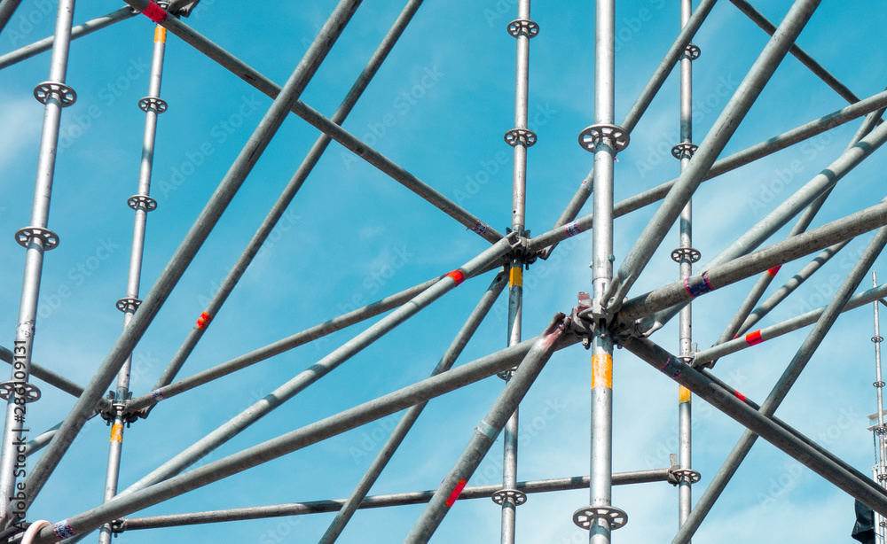 Fototapeta premium Metal pipe frame structure on blue sky background. Industrial construction from tubes raises upwards. Building process and joining elements view. Straight and inclined lines backdrop