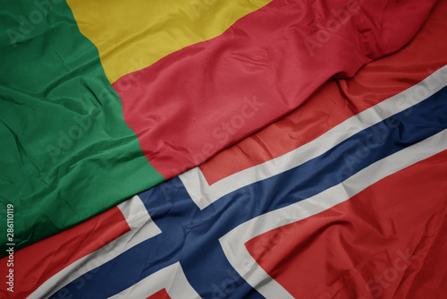 waving colorful flag of norway and national flag of benin.