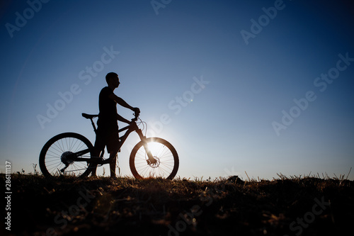 The silhouette of a bicycle and rider against the blue sky at sunset