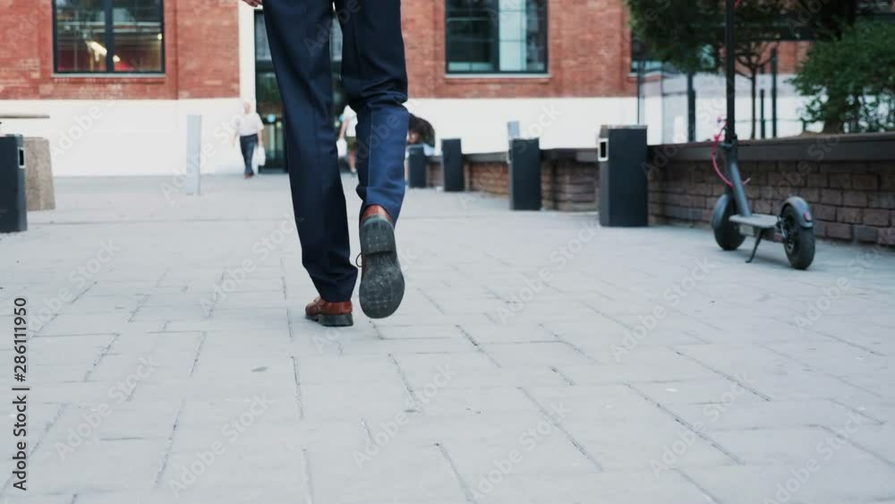 Unrecognisable businessman feet walking in the business district, back view tracking shot Unrecognisable businessman feet walking in the business district, back view tracking shot