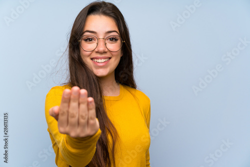 Teenager girl over isolated blue wall inviting to come photo