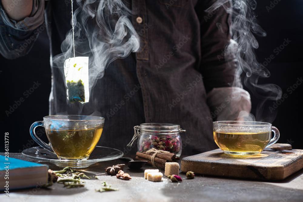 The steam from man with gray jecket is soaking tea bag on vintage white cup, preparing hot tea.Dipping teabag on cup,hot food and healthy meal concept The steam from man with gray jecket is soaking tea bag on vintage white cup, preparing hot tea.Dipping teabag on cup,hot food and healthy meal concept