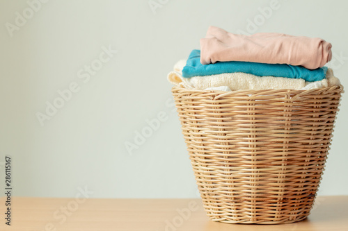 Wicker laundry basket with clean clothes with copy space on wood table against gray background. Space for text or product. 
