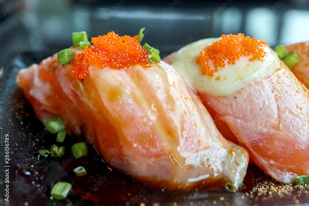 Closeup colorful Salmon Sushi with tobiko eggs on top in black plate on the black table background. Japanese Foods concept. Dark tone. Closeup colorful Salmon Sushi with tobiko eggs on top in black plate on the black table background. Japanese Foods concept. Dark tone.