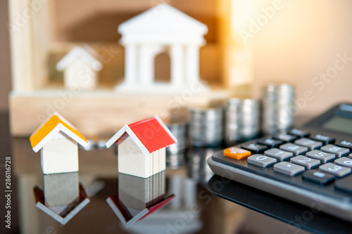 Banking concept. Loan interest rate calculation. Saving money for property investment or real estate development. Home mortgage and lease. Coin stacked, house and bank models with calculator on table. photo