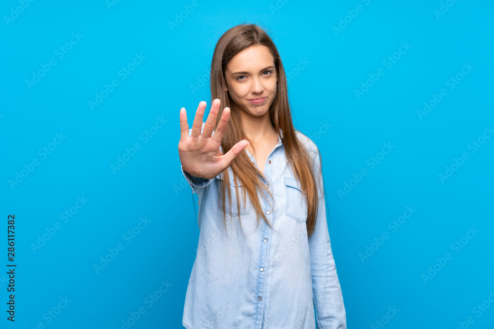 Young woman over isolated blue background making stop gesture Young woman over isolated blue background making stop gesture