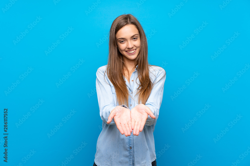 Young woman over isolated blue background holding copyspace imaginary on the palm to insert an ad Young woman over isolated blue background holding copyspace imaginary on the palm to insert an ad