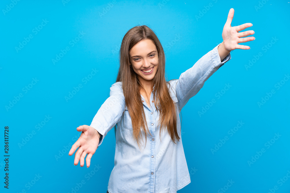 Young woman over isolated blue background presenting and inviting to come with hand Young woman over isolated blue background presenting and inviting to come with hand