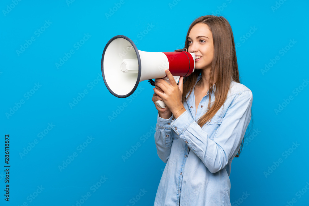Young woman over isolated blue background shouting through a megaphone Young woman over isolated blue background shouting through a megaphone