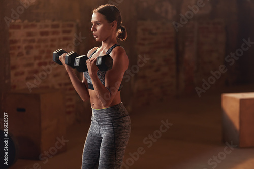 Fitness workout. Woman doing arm exercise with dumbbell at gym