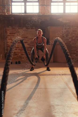 Fitness workout. Sport woman doing battle rope exercise at gym
