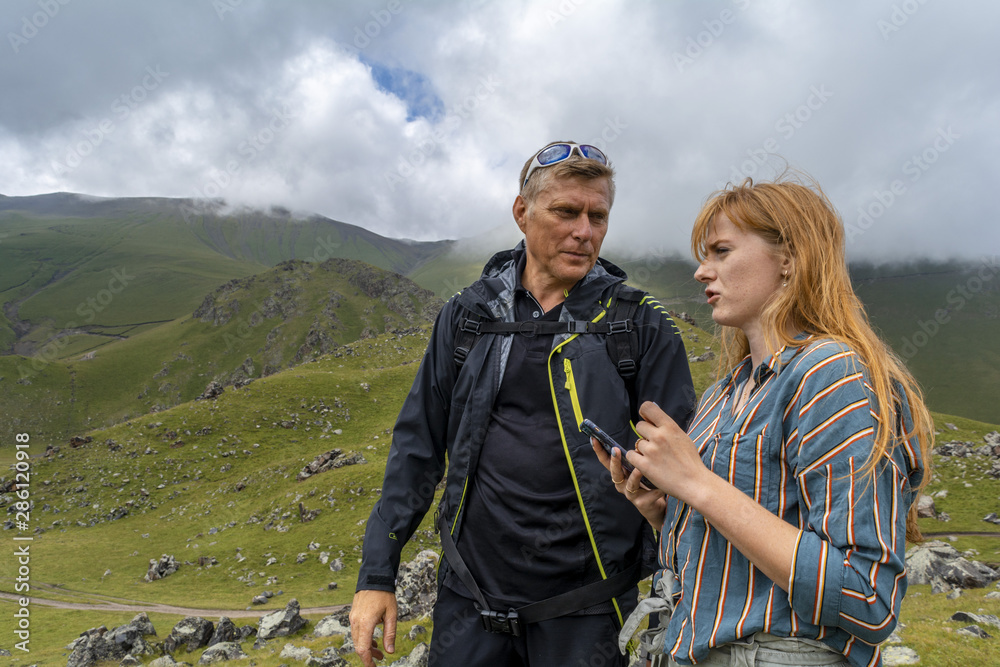 A man is talking with a girl on a beautiful background of green alpine meadow on the slopes mountains.