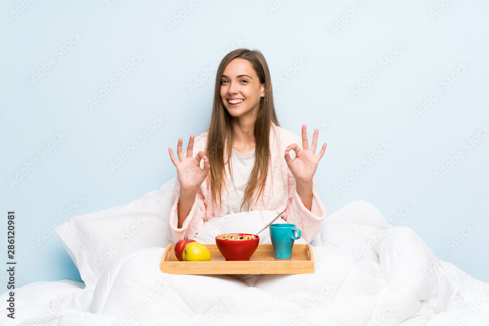 Young woman in dressing gown with breakfast showing an ok sign with fingers Young woman in dressing gown with breakfast showing an ok sign with fingers