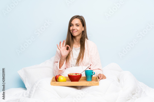 Young woman in dressing gown with breakfast showing an ok sign with fingers