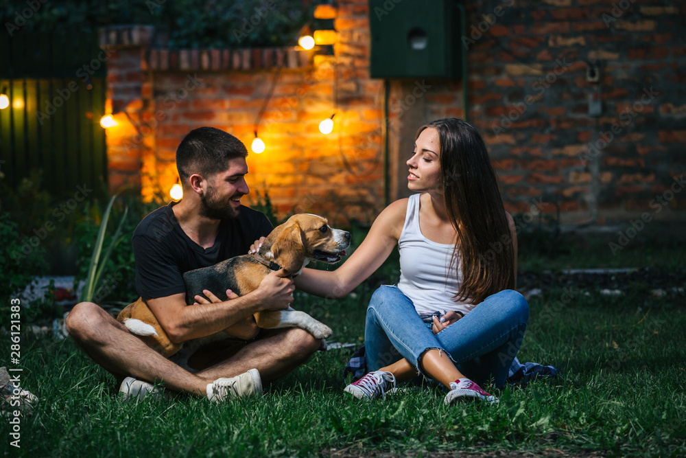 young couple playing with dog at home backyard at evening.