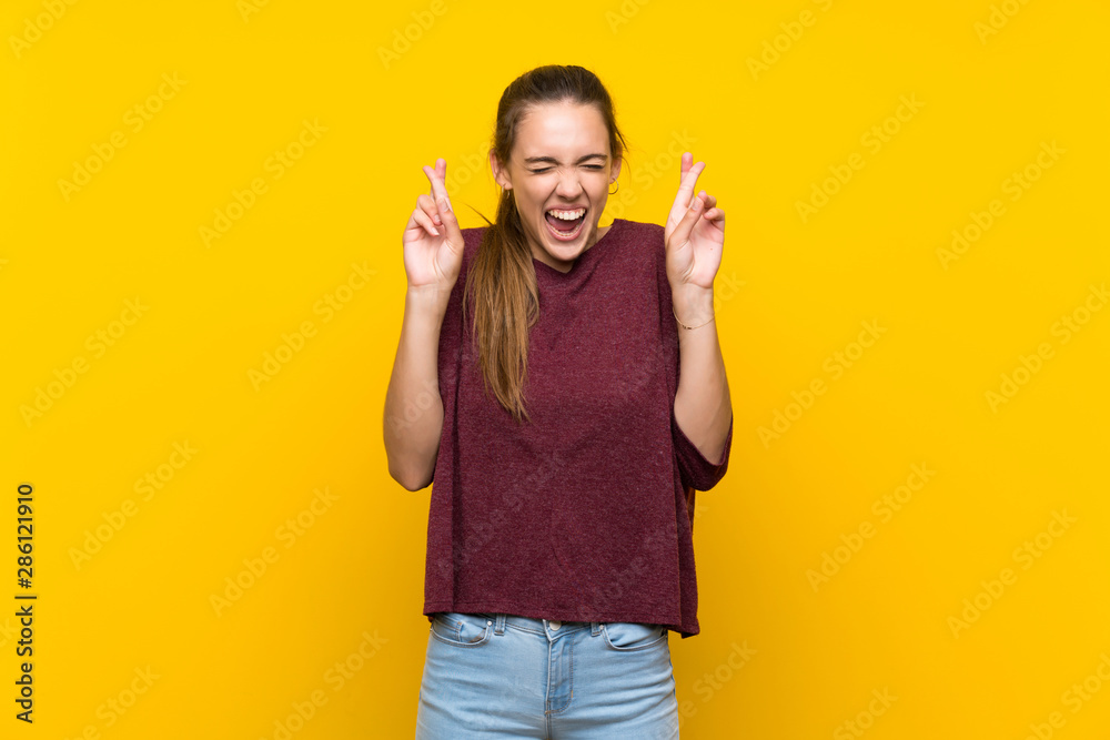 Young woman over isolated yellow background with fingers crossing Young woman over isolated yellow background with fingers crossing
