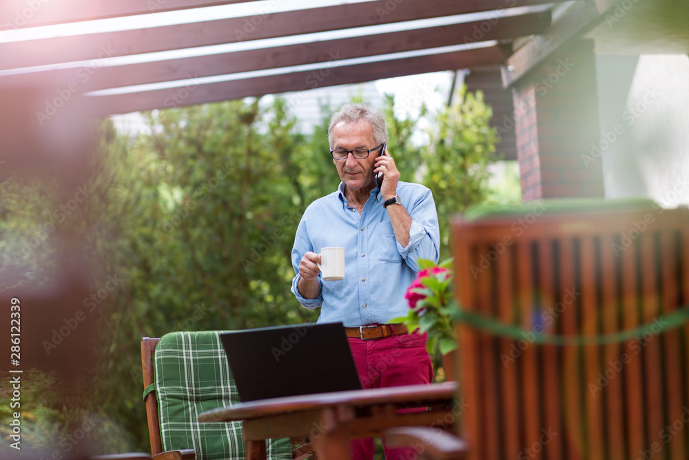 Fototapeta premium Senior man using mobile phone in backyard
