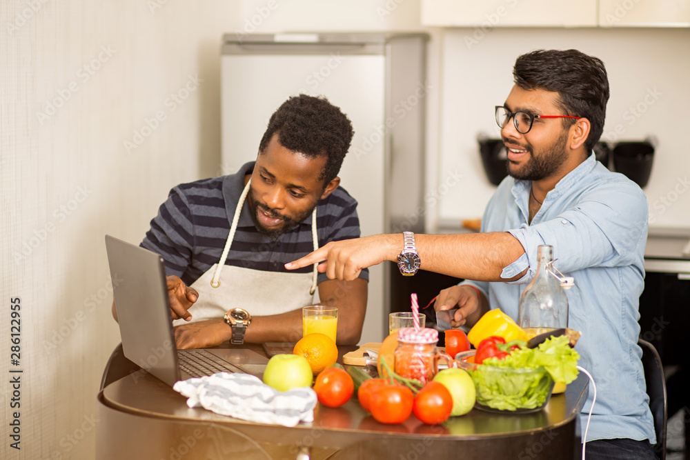 Two men using laptop in kitchen Two men using laptop in kitchen