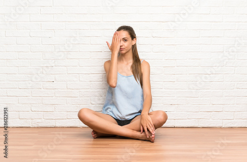 Young woman sitting on the floor covering a eye by hand