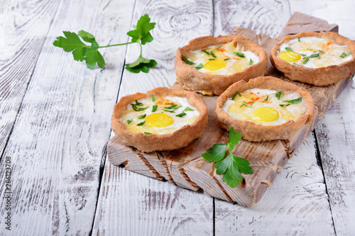 Baked rye tartlets with cheese and quail eggs on white wooden table photo