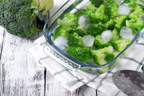Blanched broccoli cabbage cooling down in cold water in a glass dish on white table