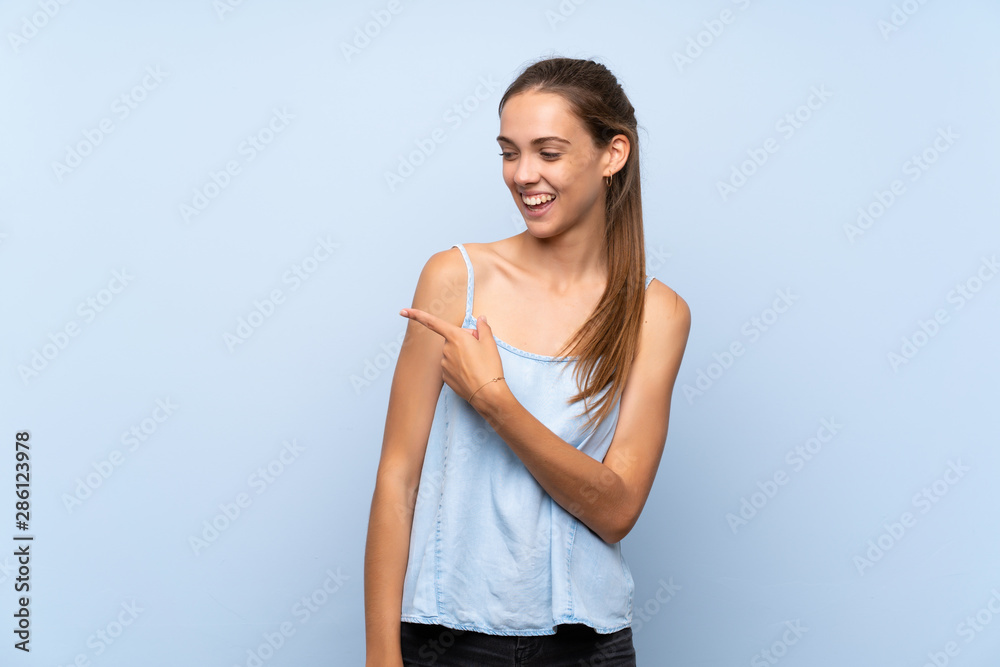 Young woman over isolated blue background pointing to the side to present a product Young woman over isolated blue background pointing to the side to present a product