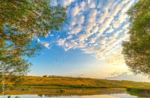 Blue sky  trees and clouds are reflected in the water.