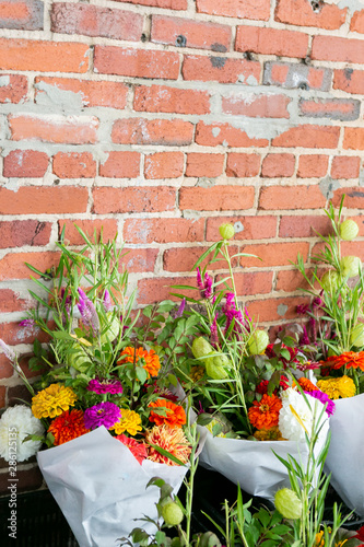 group of colorful flower bouquets at farmers market, wild flower bouquets wrapped in paper, brick background