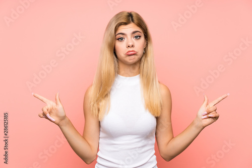 Teenager girl over isolated pink background pointing to the laterals having doubts