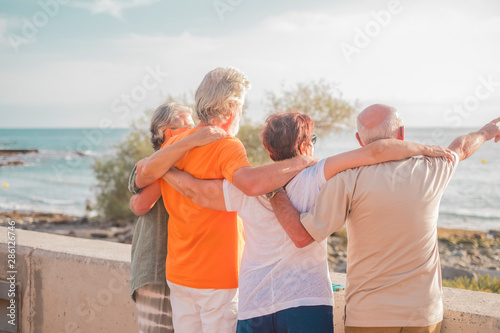 group of seniors and mature people at the beach looking the sea or the ocean hugged and one of they is indicating something