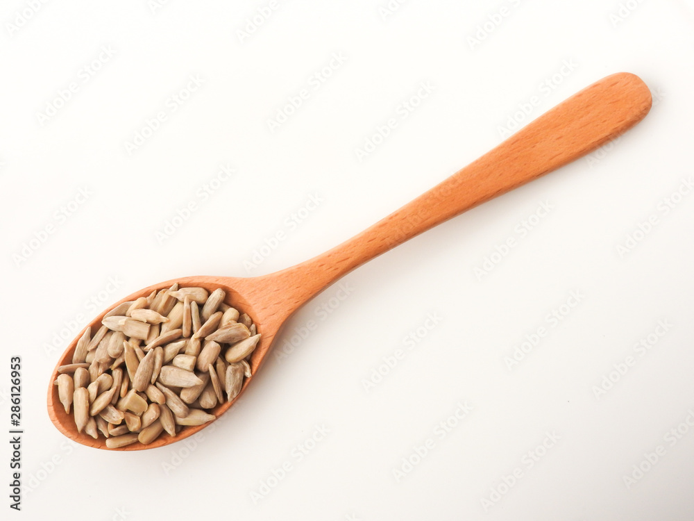 Top view of natural shelled organic sunflower seeds on wooden spoon isolated on white background. It often eaten as a snack. The seeds contain vitamin E. Food and snack concept. Top view of natural shelled organic sunflower seeds on wooden spoon isolated on white background. It often eaten as a snack. The seeds contain vitamin E. Food and snack concept.