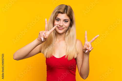 Teenager girl over isolated yellow background smiling and showing victory sign