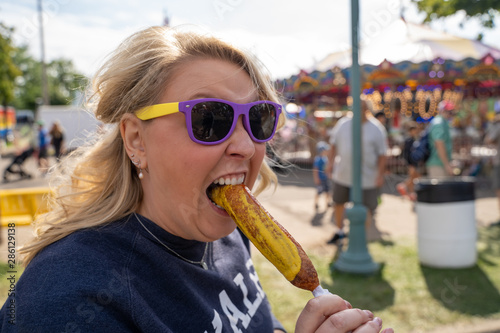 Blonde woman eats a pronto pup corn dog covered in mustard at an outdoor fair photo