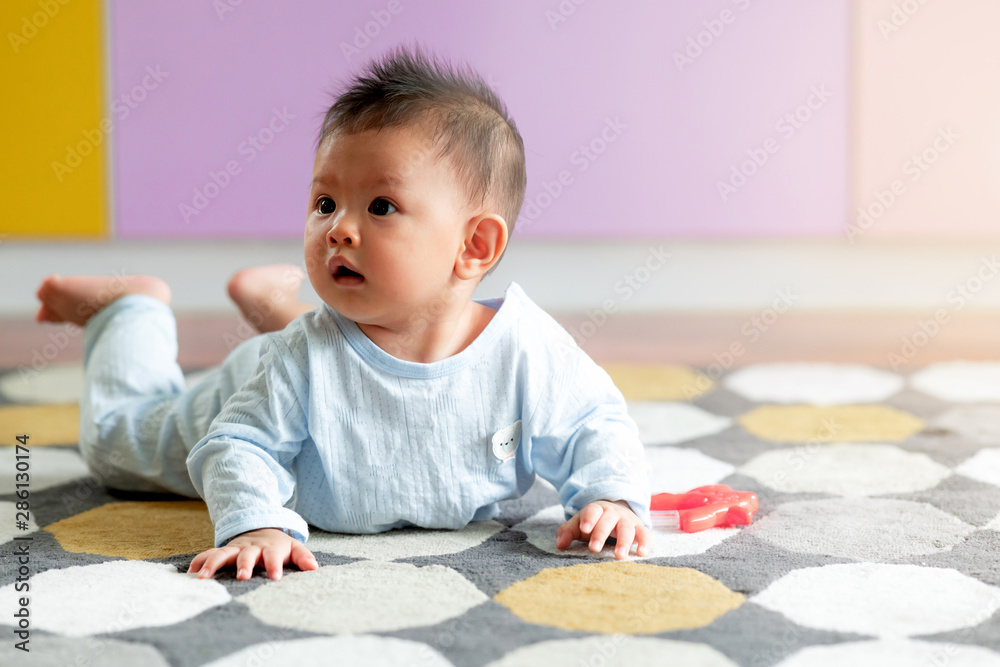 Portrait of young asian baby toddler laying on floor on carpet with colorful background. Looking to the left. With light leak effect. Portrait of young asian baby toddler laying on floor on carpet with colorful background. Looking to the left. With light leak effect.