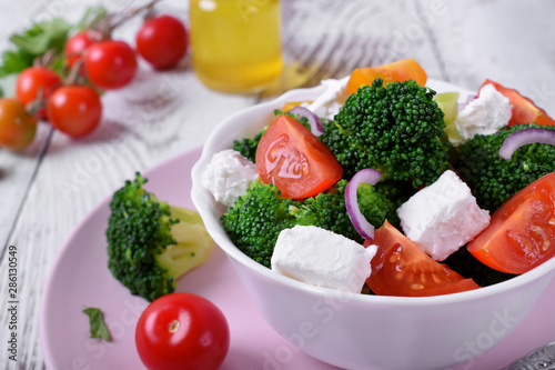 Light salad with broccoli, cherry tomatoes and feta cheese in a white ceramic bowl