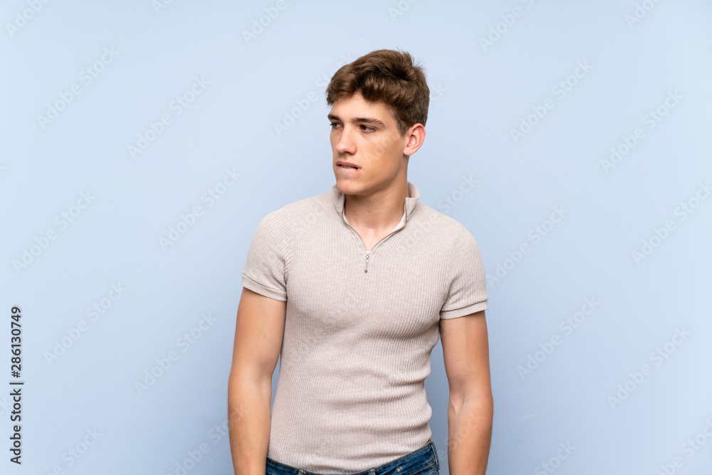Handsome young man over isolated blue wall with confuse face expression