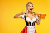 Wow emotion. Young sexy Oktoberfest girl waitress, wearing a traditional Bavarian or german dirndl, serving big beer mugs with drink isolated on yellow background.