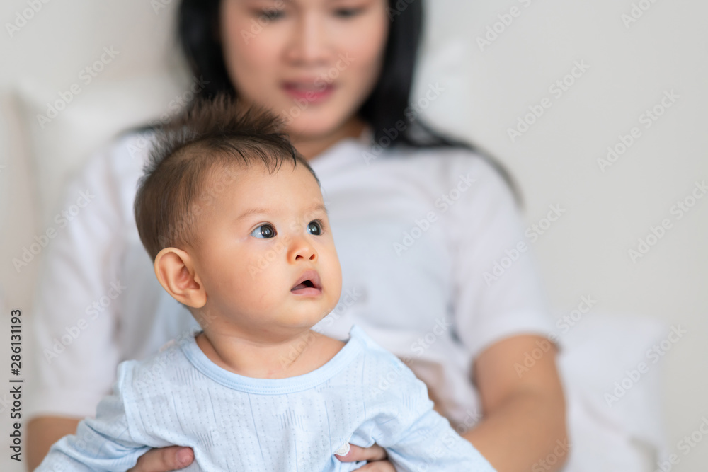 Asian male toddler sitting with his pregnant mother in bedroom. Curious look. Asian male toddler sitting with his pregnant mother in bedroom. Curious look.