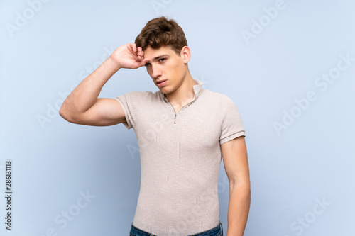 Handsome young man over isolated blue wall with tired and sick expression