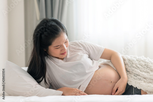 Asian pregnant woman laying in bed with open shirt. Touching her belly. With light leaks effect.
