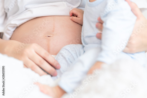 Asian male toddler sitting with his pregnant mother in bedroom. Close up shot.