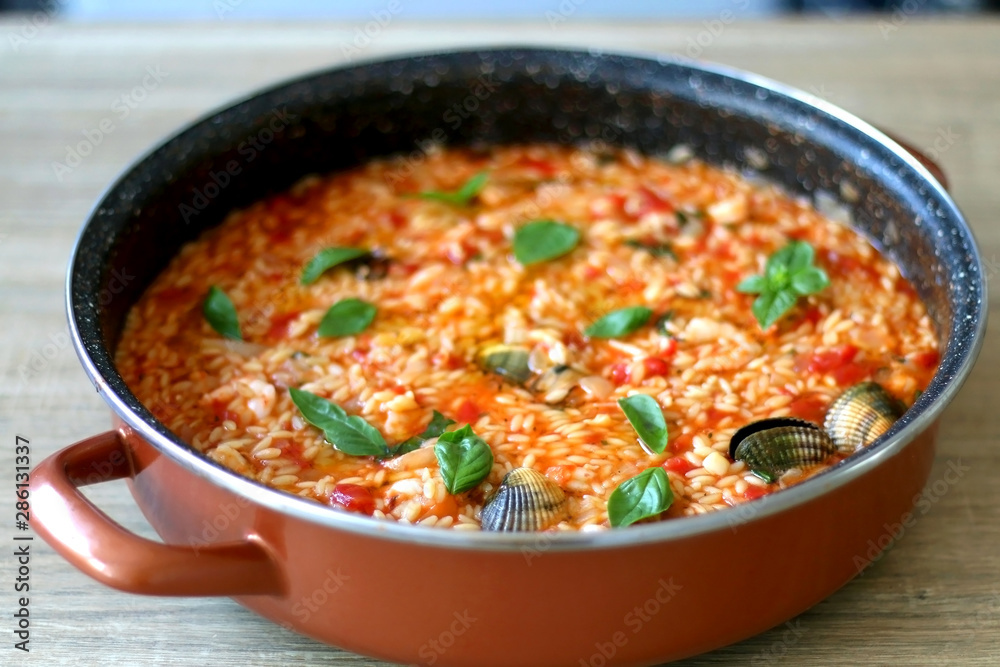 Orzo pasta, cooked with tomato sauce, vegetables and seafood, served on a table. Selective focus. Orzo pasta, cooked with tomato sauce, vegetables and seafood, served on a table. Selective focus.