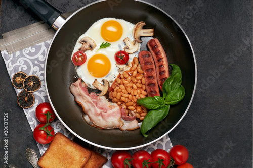English breakfast. Fried eggs, sausages, bacon, beans, toasts, tomatoes on stone table. Top view with copy space