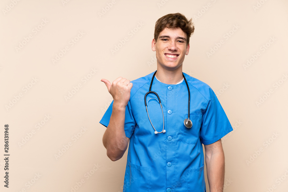Surgeon doctor young man over isolated wall pointing to the side to present a product Surgeon doctor young man over isolated wall pointing to the side to present a product