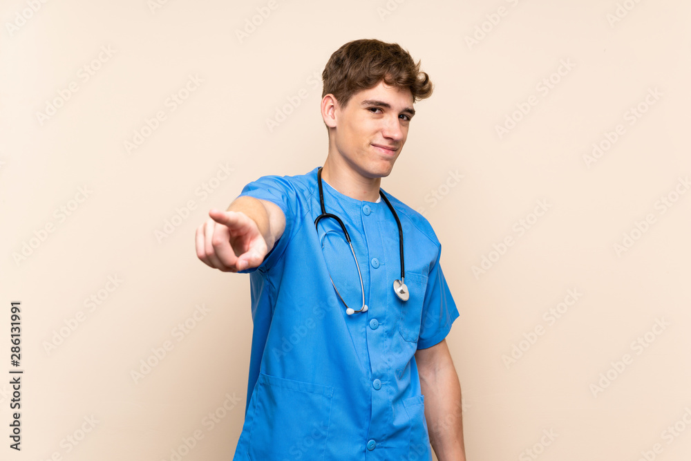 Surgeon doctor young man over isolated wall points finger at you with a confident expression Surgeon doctor young man over isolated wall points finger at you with a confident expression
