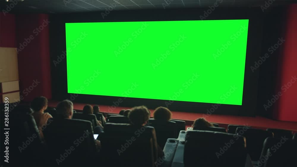 Viewers people are enjoying interesting movie on big green screen copyspace in dark cinema looking with attention. Template, entertainment and films concept.