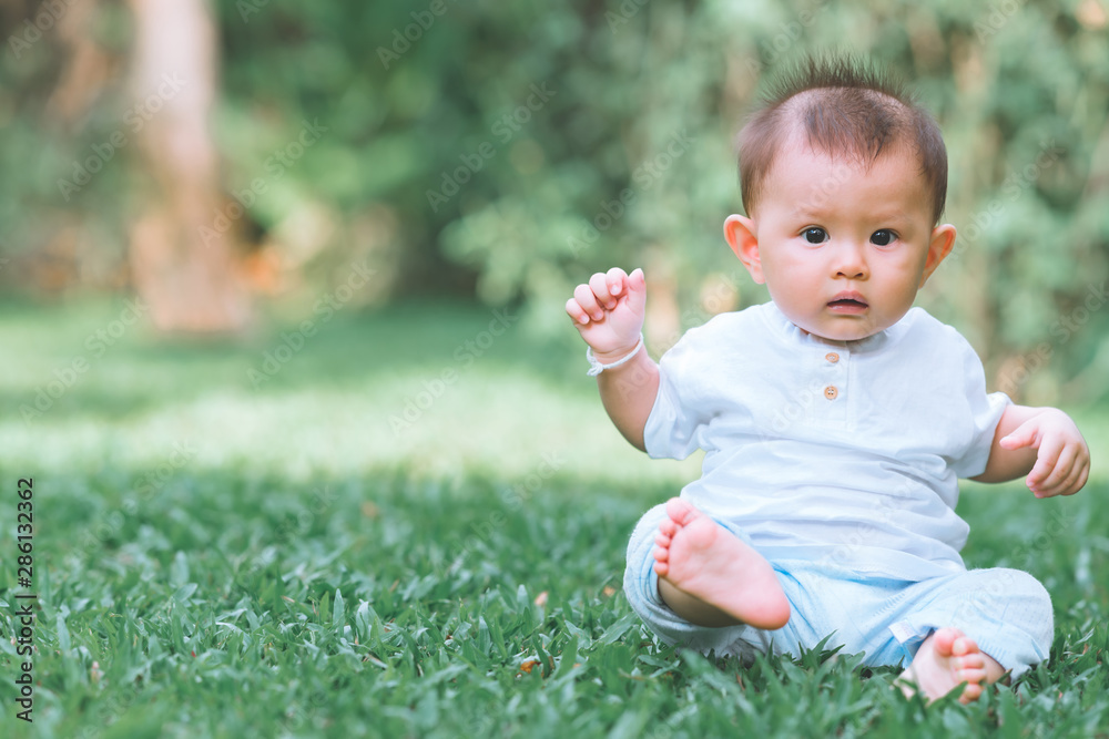 Asian male toddler sitting on grass in park. With copy space, worry look. Asian male toddler sitting on grass in park. With copy space, worry look.