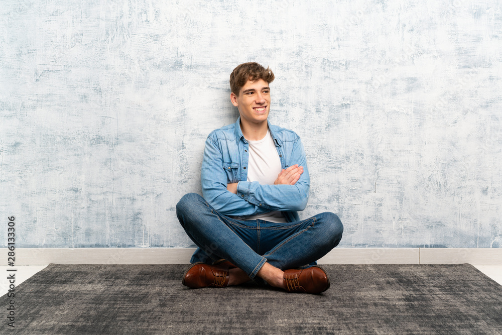 Handsome young man sitting on the floor laughing Handsome young man sitting on the floor laughing