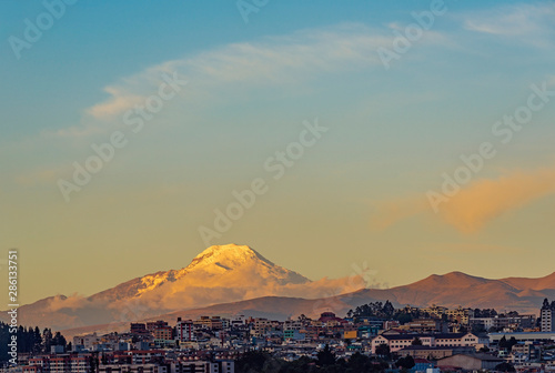 The snowcapped Andes peak of the Cayambe volcano at sunset with the urban skyline of Quito, Ecuador.